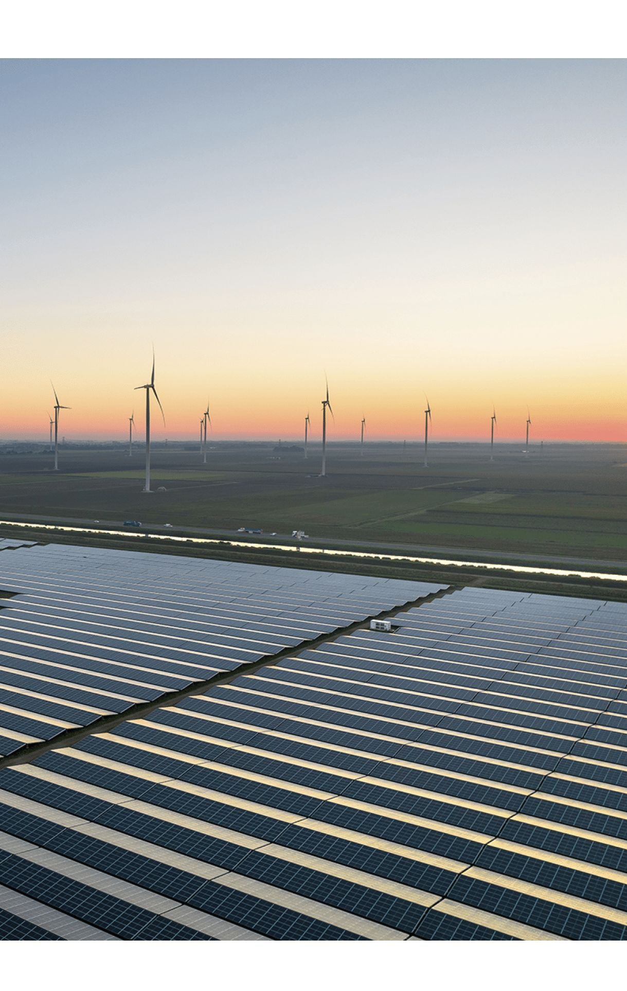 Aerial view from a drone of a solar panel field surrounded by wind turbines during a summer sunrise.  Groningen, the Netherlands, September 2023