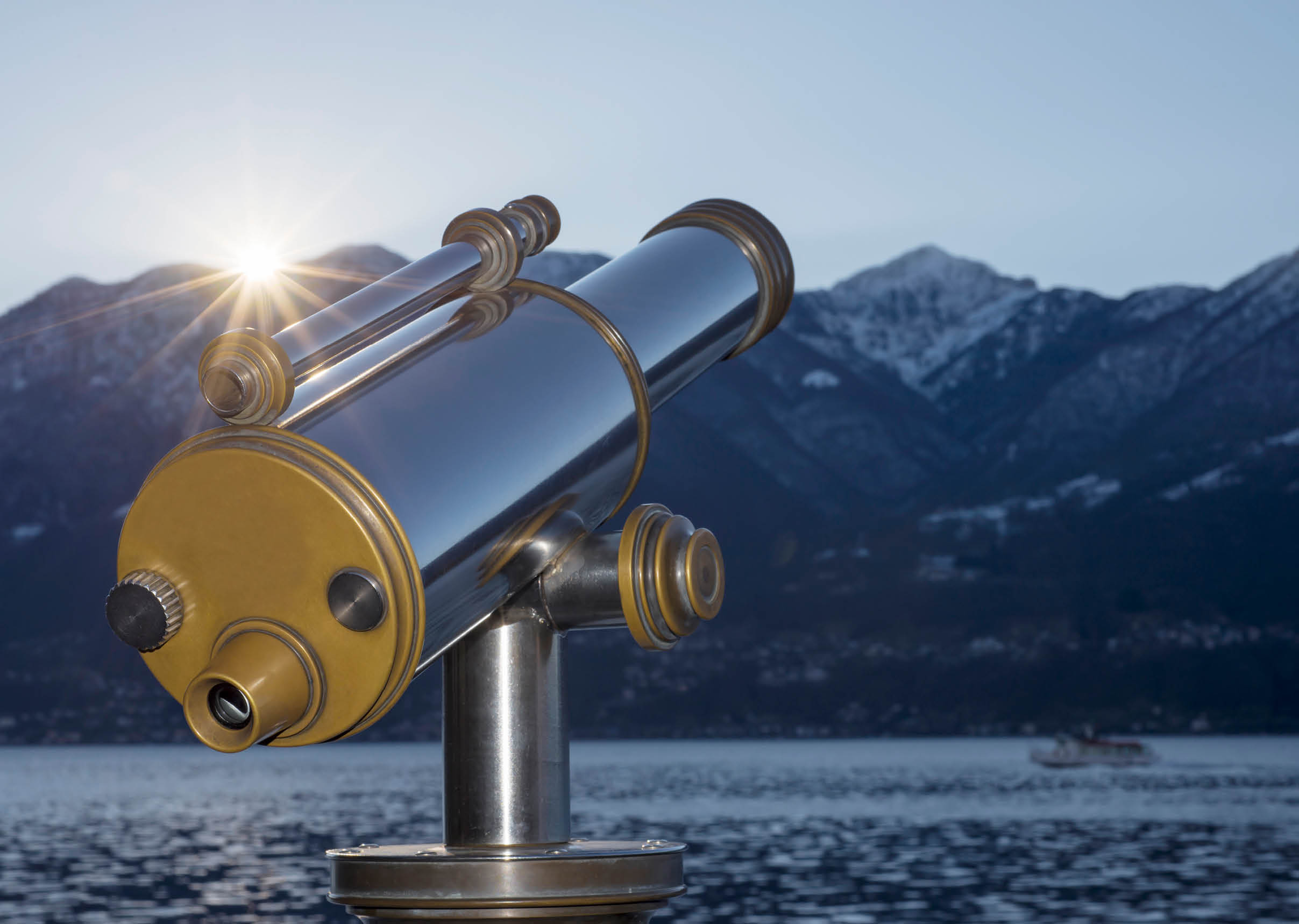 Telescope in sunrise over an alpine lake maggiore with snow-capped mountains in Ticino, Switzerland.